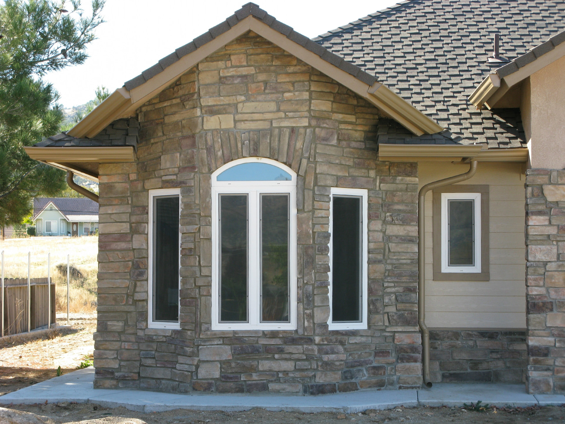 Stone-faced Tehachapi area home with tan seamless gutters and a rounded downspout