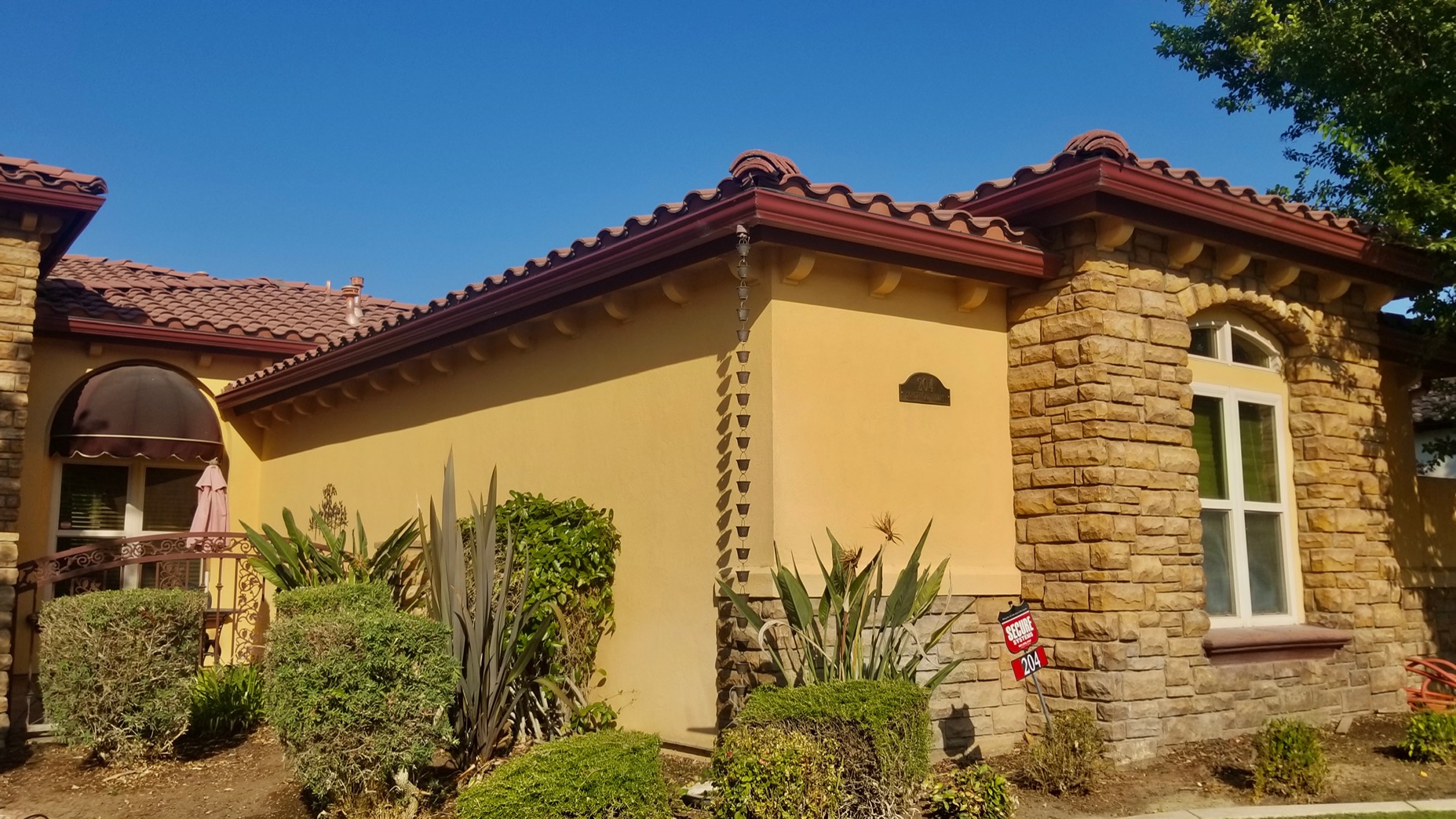 Spanish style Kern River Valley home with dark red fascia gutters and a rain chain downspout