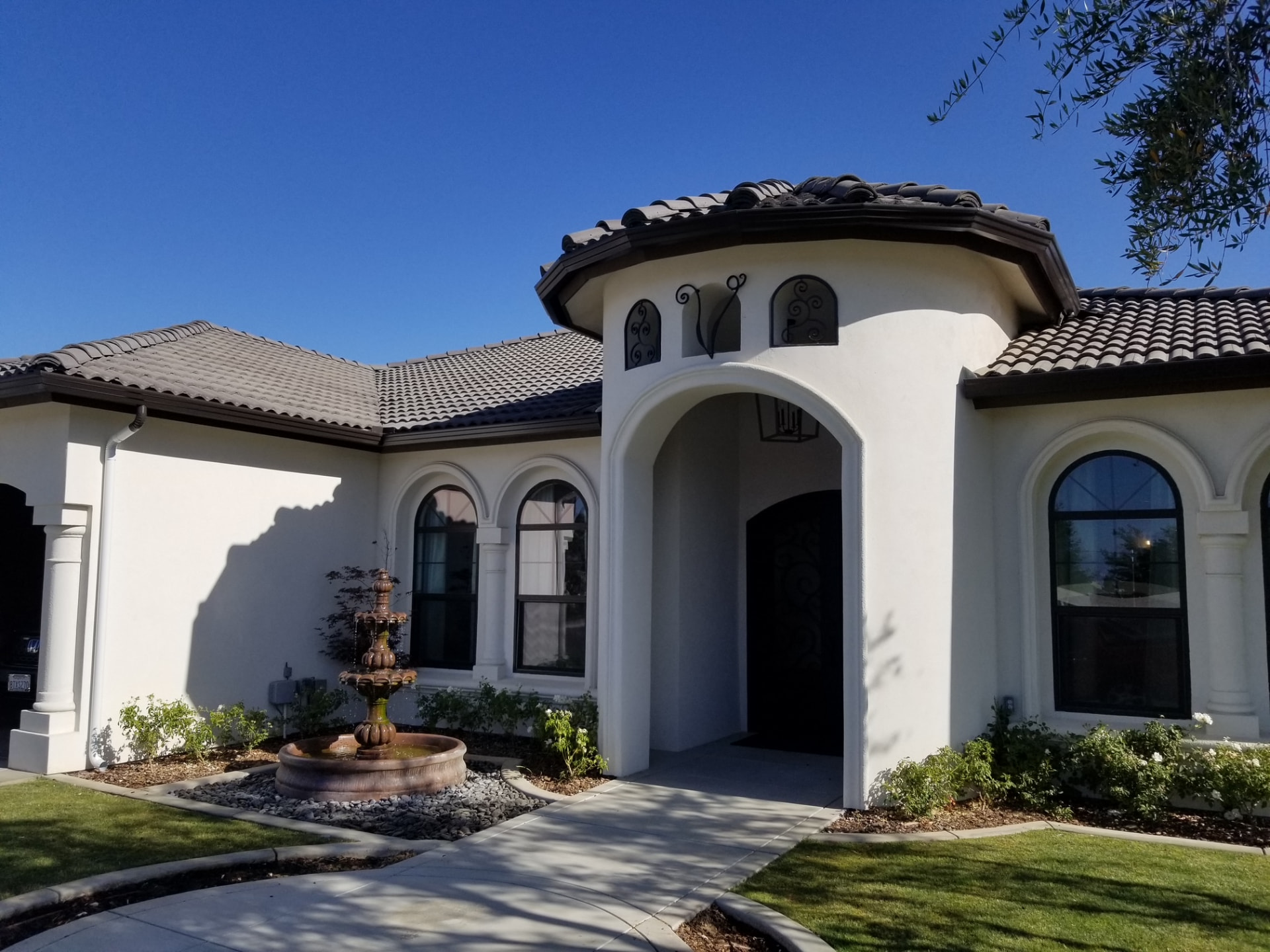 White stucco home with an arched entry, fountain and dark seamless gutters near Visalia