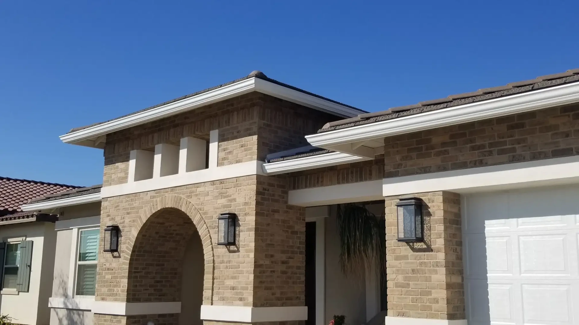 Brick home with white seamless rain gutters along the roofline and arched entry