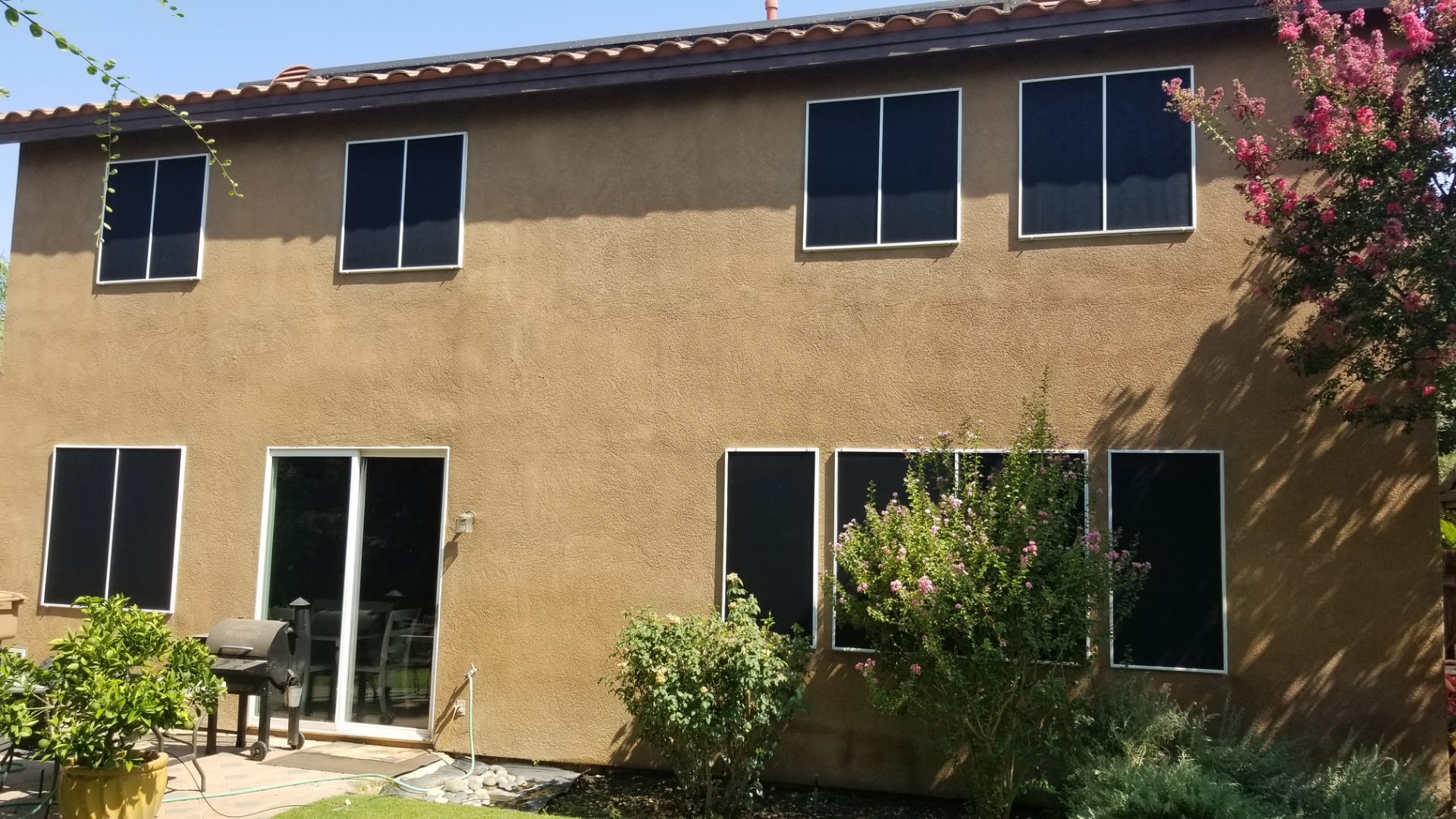 Two-story stucco home with black sunscreens on every window and patio slider